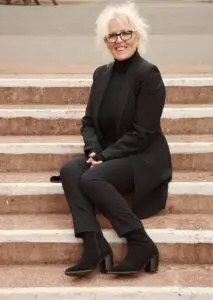 A picture of Paula C Whitfield founder and hypnotherapist or Lose Weight Be Happy and Ambiance Hypnotherapy, Paula is sitting down smiling on some steps wearing a black suit.